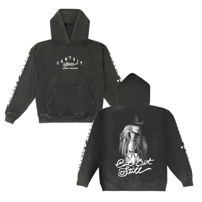 Black hoodie featuring a white graphic print of lainey wilson and the text ‚Äôcan‚Äôt sit still‚Äô on both front and back, with star patterns along the sleeves.