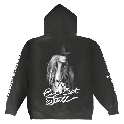 Black hoodie featuring a black-and-white graphic of a woman in a cowboy hat with the text ‚Äôcan‚Äôt sit still‚Äô printed below.